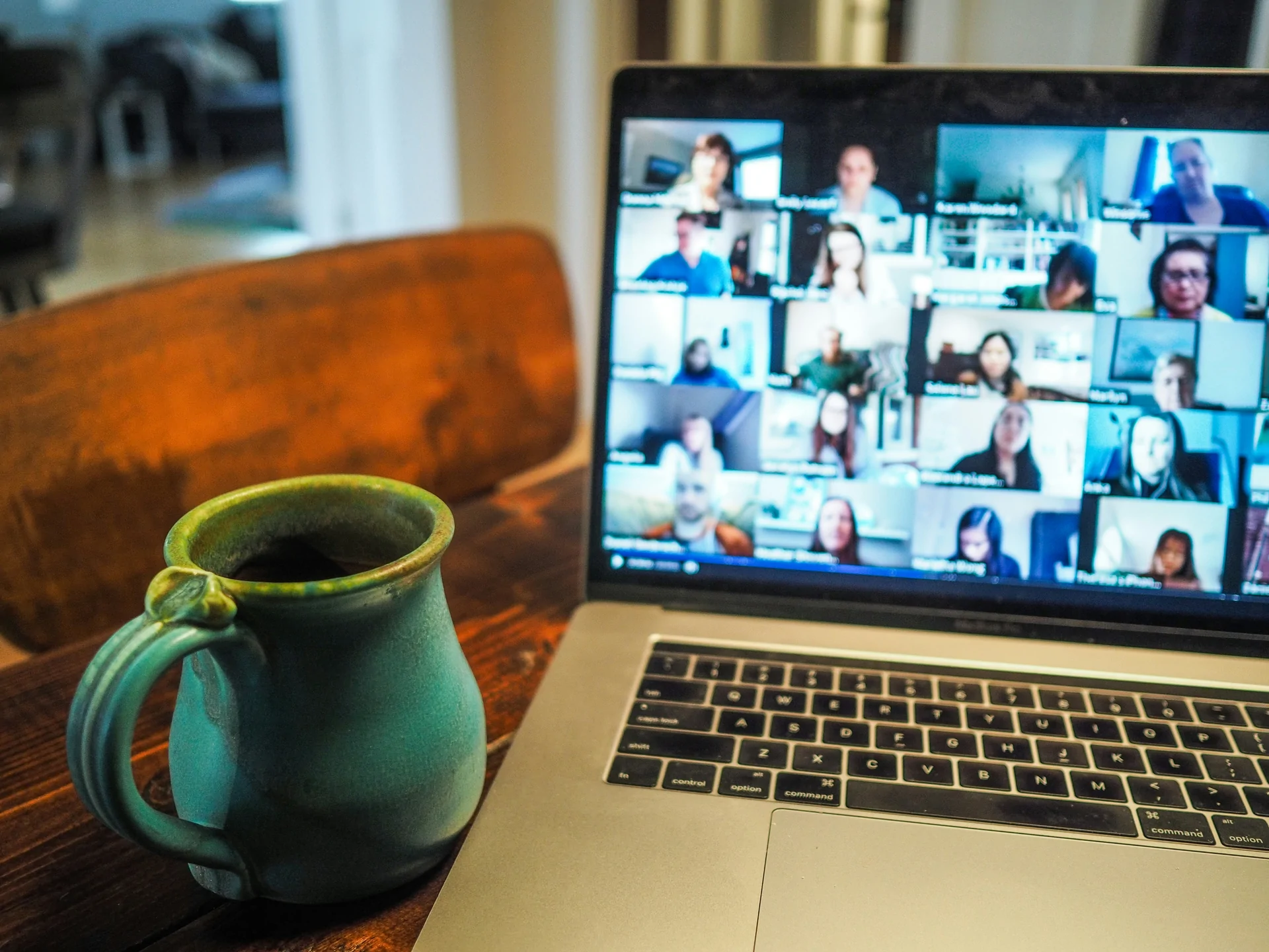 A laptop displaying participants in an online workshop beside a mug